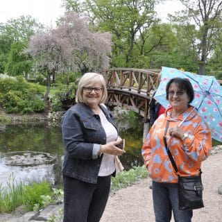 Dwie uśmiechnięte panie w ogrodzie botanicznym, jedna z nich trzyma parasol