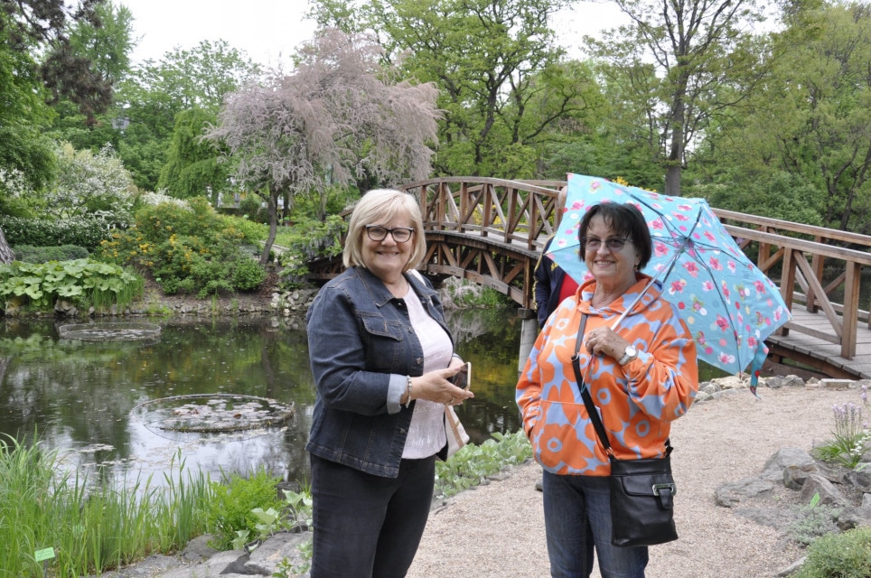 Dwie uśmiechnięte panie w ogrodzie botanicznym, jedna z nich trzyma parasol