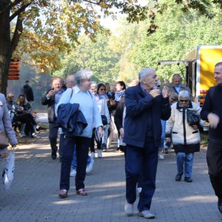 Grupa seniorów idzie chodnikiem między drzewami