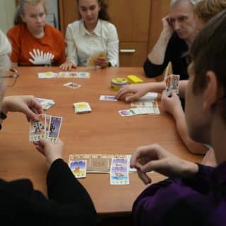 Kilka osób z kartami siedzi wokół stołu. Przed każdym leży kilka kart