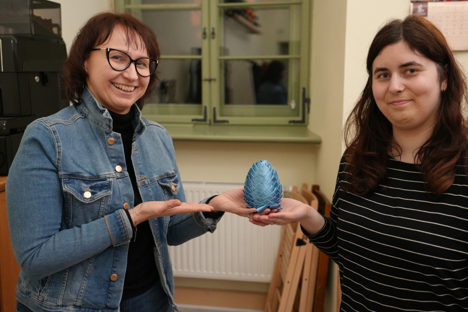 Dwie kobiety wskazują na jajko wielkanocne zrobione z niebieskiej wstążki