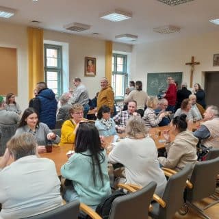 Kilkadziesiąt osób w sali przy stolikach z kawą, herbatą i ciastkiem