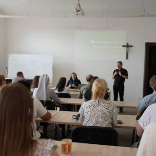 Grupa osób podczas zajęć na sali wykładowej, obok prowadzącej zajęcia tłumacz języka migowego