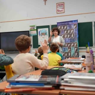 Sala szkolna, dzieci w ławkach naśladują migającą nauczycielkę przy tablicy