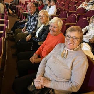 Kilkoro seniorów siedzi na widowni teatralnej na fotelach obok siebie