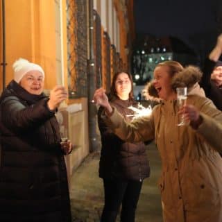 Kilka osób ze sztucznymi ogniami i lampką szampana na tle budynku