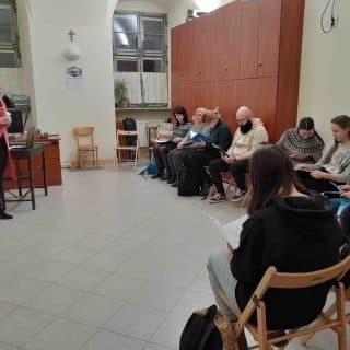 Grupa osób siedzi w sali w półokręgu przed lektorką