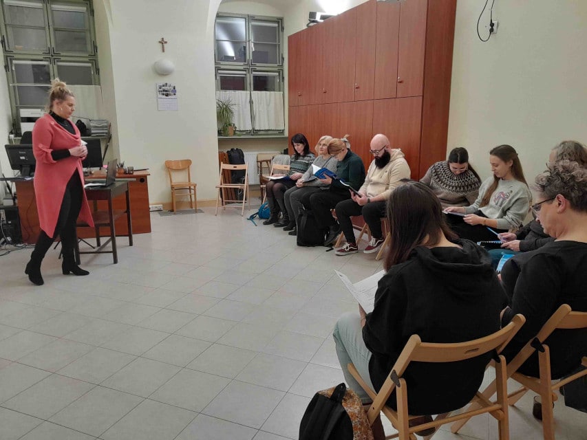 Grupa osób siedzi w sali w półokręgu przed lektorką