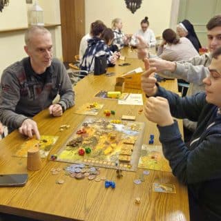 Przy długim stole w dwóch grupach grają w gry planszowe