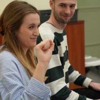 Migająca kobieta w sali, w tle spoglądający na nią mężczyzna