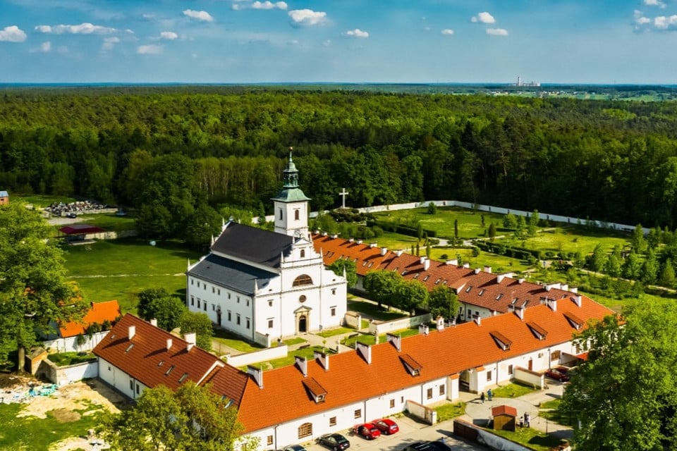 Kościół otoczony zabudowaniami klasztornymi na skraju lasu