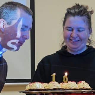 Mężczyzna dmucha w świeczki umieszczone na cieście trzymanym przez kobietę