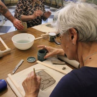 Kobieta z aparatem słuchowym pracuje przy stoliku podczas warsztatów rękodzieła