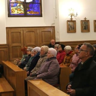 Grupa osób siedzi w kościelnych ławkach