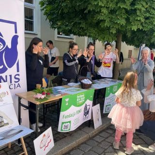 Kilka osób przy plenerowym stoisku z wolontariuszami Fundacji FONIS