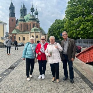 Cztery osoby pozują do zdjęcia na moście na tle katedry w Poznaniu