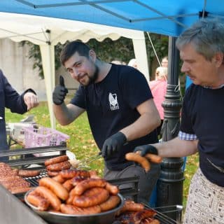 Mężczyźni grillują kiełbasę na dużym ruszcie pod namiotem