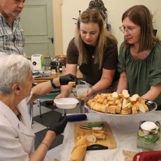 Dwie kobiety częstują seniorkę chlebem i oliwą