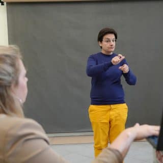 Migająca kobieta na szarym tle. Przed nią kobieta z laptopem skierowanym ku migającej