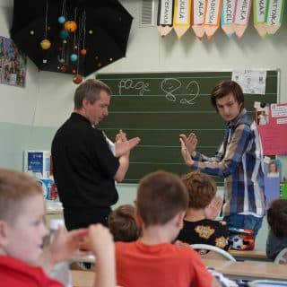 Dwóch migających mężczyzn przy tablicy w sali lekcyjnej z uczniami