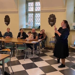 Stojąca na środku sali kobieta miga do siedzących przy stolikach ludzi