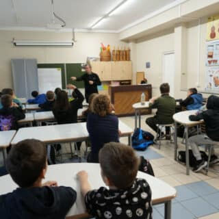 Mężczyzna na środku sali lekcyjnej pośród zgłaszających się dzieci