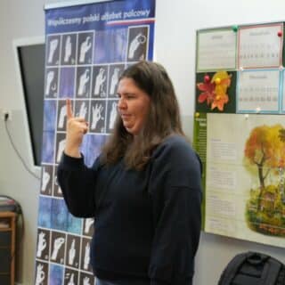 Migająca kobieta przy planszy z alfabetem języka migowego