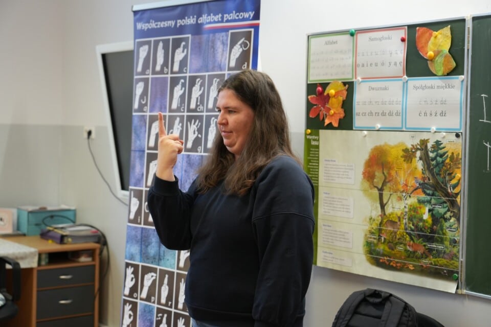 Migająca kobieta przy planszy z alfabetem języka migowego