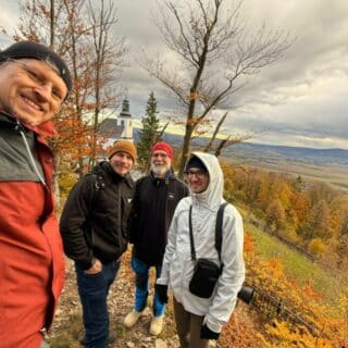 Czterech mężczyzn na tle jesiennego krajobrazu z drzewami, górami i kościołem