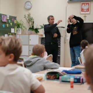 Dwóch mężczyzn w sali lekcyjnej pokazuje dzieciom implant ślimakowy