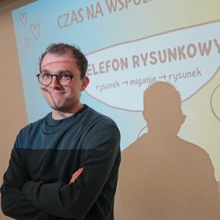 Uśmiechnięty mężczyzna w okularach na tle obrazu z rzutnika