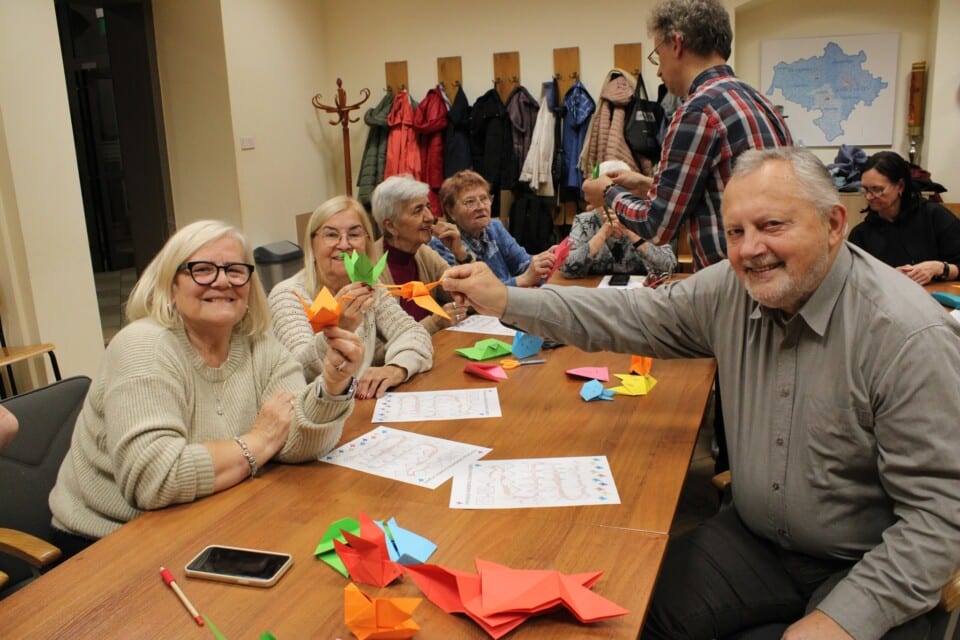 Kilka osób przy stole prezentuje papierowe ozdoby origami