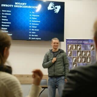 Uśmiechnięty mężczyzna pod ekranem z listą słów i migającymi dłońmi