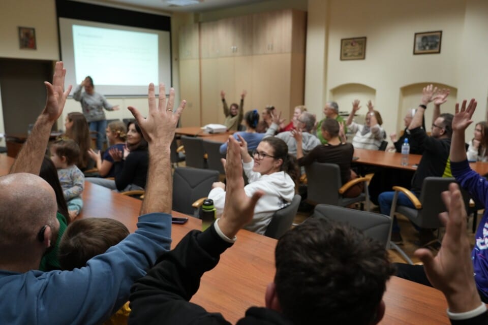 Kilkadziesiąt osób siedzących w sali podnosi ręce do góry