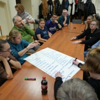 Kilkanaście osób wokół dużego arkusza papieru na długim stole