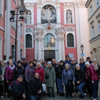 Kilkadziesiąt osób pozuje do zdjęcia grupowego na tle kościoła