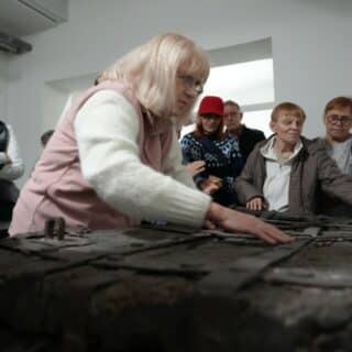 Kilka osób niewidomych dotyka metalowe okucia starej drewnianej skrzyni