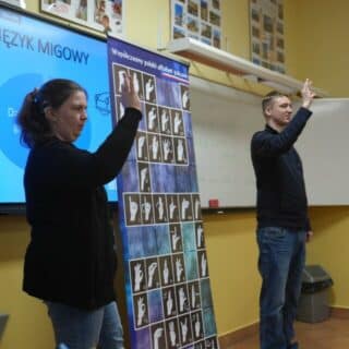 Migająca kobieta i mężczyzna przy tablicy z alfabetem migowym