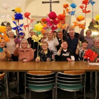 Kilkanaście osób w sali pozuje do zdjęcia z dużymi papierowymi kwiatami