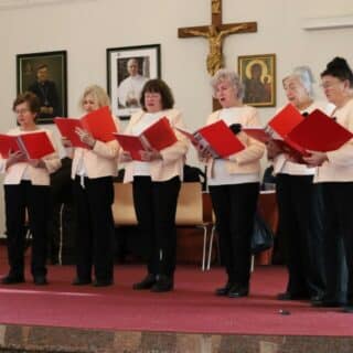 Sześć jednakowo ubranych kobiet z czerwonymi teczkami podczas śpiewu