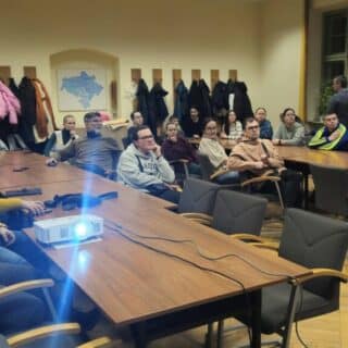 Grupa ludzi siedzi przy stolikach w dużej sali