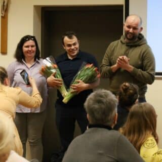 Między mężczyzną i kobietą stoi mężczyzna z dwoma bukietami tulipanów
