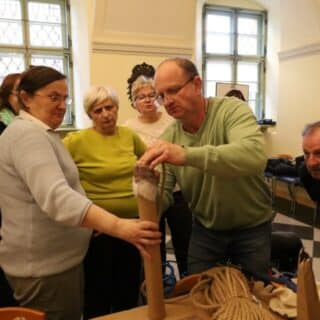 Kilkoro seniorów patrzy na mężczyznę przyklejającego sznur do tekturowej rury