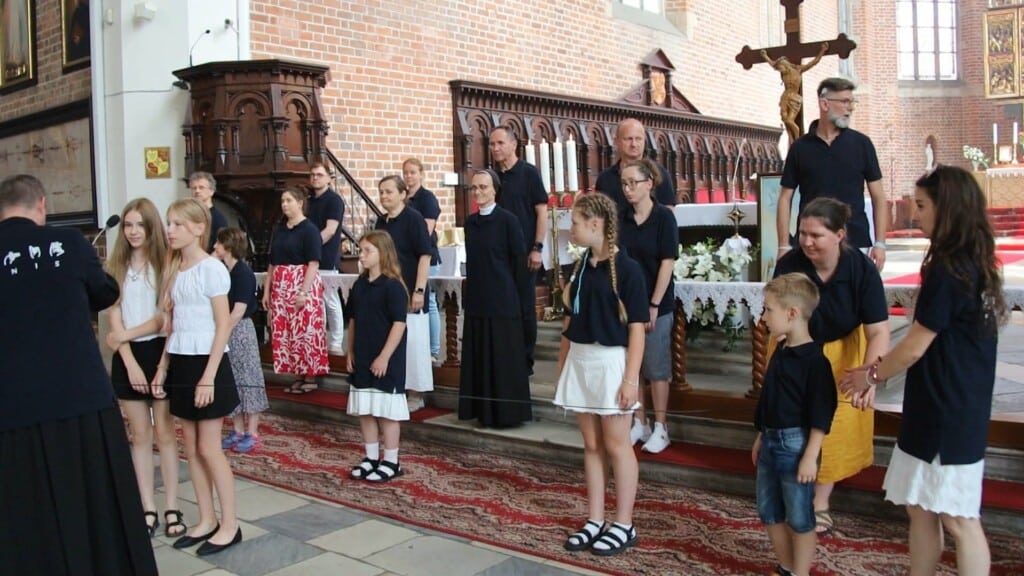 W kościele przed ołtarzem ludzie ustawieni w trzech rzędach
