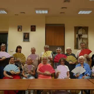 Grupa seniorów z wachlarzami w sali pozuje do zdjęcia