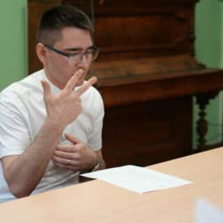 Migający mężczyzna przy stoliku patrzy na leżącą przed nim kartkę