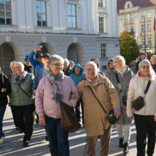Grupa seniorów na rynku na tle zabudowań z ratuszem na środku